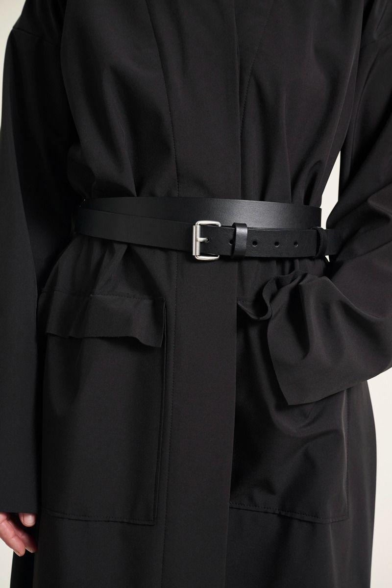 Schwarzer Ledergürtel mit einer Silberschnalle von BITTE KAI RAND, tailliert getragen über einer schwarzen Jacke oder einem Kleid mit Taschen.